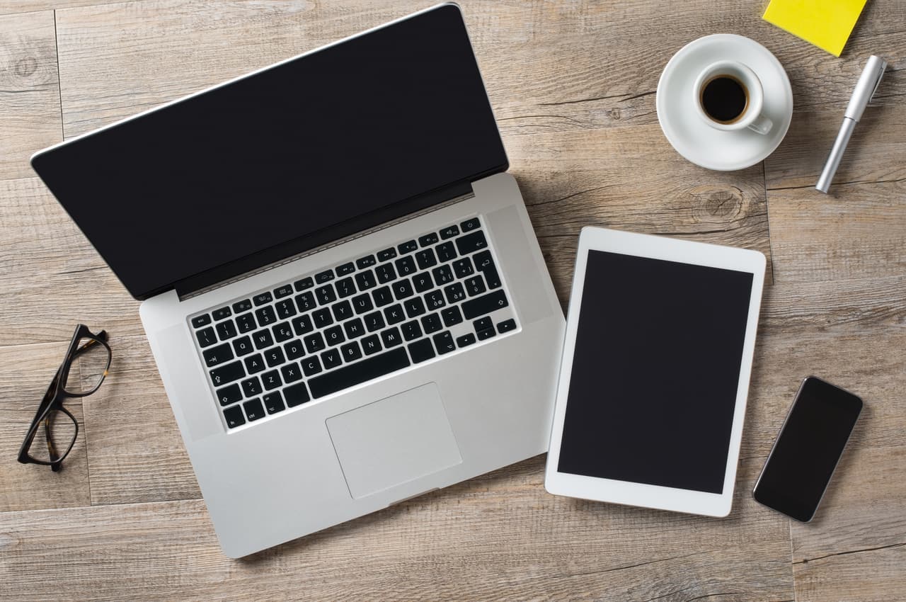 Modern laptop, tablet, smartphone, eyeglasses, coffee cup, and pen on a wooden desk, illustrating remote work and digital communication tools for SEO-optimized imagery.