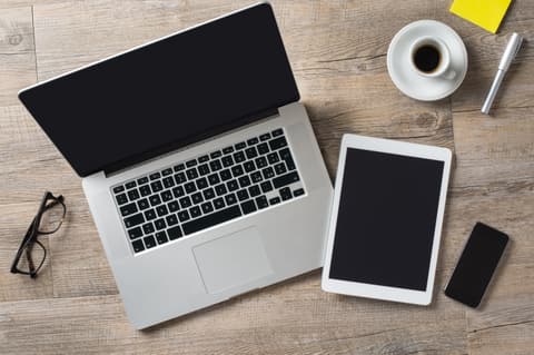 Modern laptop, tablet, smartphone, eyeglasses, coffee cup, and pen on a wooden desk, illustrating remote work and digital communication tools for SEO-optimized imagery.